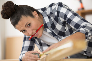 girl measuring wood with pencil held between her teeth