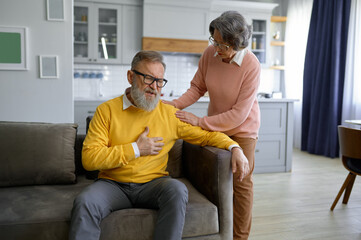 Senior man touching chest having heart attack and his wife supporting him