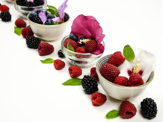 Small bowls with flowers of mallow tree, raspberries, blackberries and blueberries on a white table