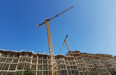 Yellow construction crane against the blue sky background Monolith from the concrete background