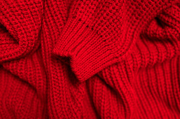 Texture of knitted woolen red sweater. Cotton wool acrylic cashmere sweater. Soft texture of fabric folds, cozy bright clothes background. Closeup textile