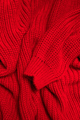 Texture of knitted woolen red sweater. Cotton wool acrylic cashmere sweater. Soft texture of fabric folds, cozy bright clothes background. Closeup textile