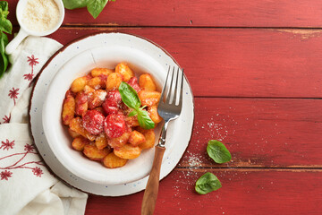 Potato gnocchi. Traditional homemade potato gnocchi with tomato sauce, basil and parmesan cheese on red rustic kitchen table background. Traditional Italian food. Top view.