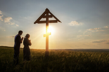 Woman and man praying outdoors at the Christian Cross. On the background of the sunset sky.