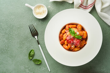 Potato gnocchi. Traditional homemade potato gnocchi with tomato sauce, basil and parmesan cheese on kitchen table on light green kitchen table background. Traditional Italian food. Top view.