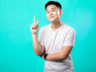 A portrait of an Asian man wearing a white t-shirt, posing as if having a brilliant idea with his finger pointing upwards, isolated with a turquoise background.