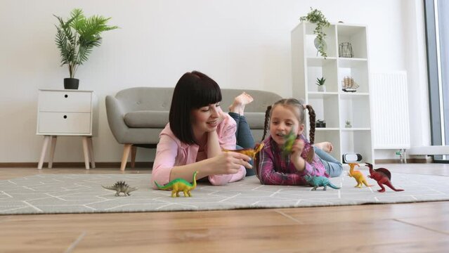 Close up view of affectionate mother and curious child being engaged in dinosaur play of plastic toys in lounge. Caring female parent sparking daughter's creativity by building own imaginary world.