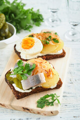 Open sandwich or smorrebrod with rye bread, herring, eggs, caramelized onions, parsley and cottage cheese on old wooden rustic table backgrounds. Danish or Scandinavian traditional food snack lunch.