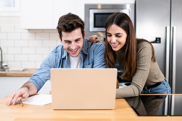 young couple planning vacations together at home looking a laptop. two cheerful young adults sitting on the kitchen. finance concept