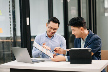 Two Asian business workers talking on the smartphone, tablet and using laptop at the office.