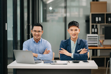 Two Asian business workers talking on the smartphone, tablet and using laptop at the office.