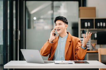 Business asian man Talking on the phone and using a laptop with a smile while sitting at modern office