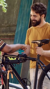 Vertical video Athletic man adjusting bike on repair-stand for repairing in home yard with african american lady. Sporty caucasian boyfriend receiving help from girlfriend in realigning bicycle