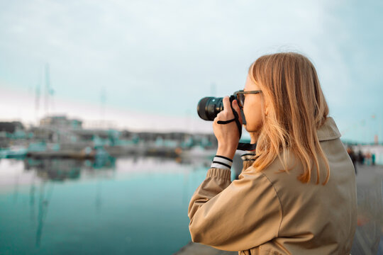 Outdoor summer smiling lifestyle portrait of pretty young woman having fun in the city in Europe in evening with camera travel photo of photographer. Making pictures on the pier near the expensive