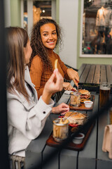 Two girls are sitting in the cafe and eating delicious burgers, french fries and drinking beers.