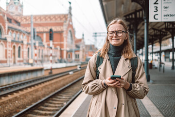 Young cry blonde woman crying and waiting train on station platform. She lost and using smart...
