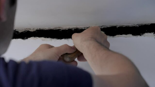 Builder installer repairs joint of plates. Finisher repairs cracks in apartment at home, is sealed with a spatula and an adhesive sealant with additives for better adhesion