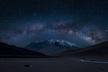 Bow-shaped Milky Way arches above a round peak. The night sky comes alive with the cosmic embrace of stars, offering a glimpse into the mesmerizing beauty of Ladakh's nighttime realm - obrazy, fototapety, plakaty