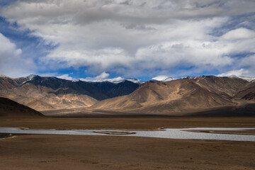 Naklejka premium Silently coursing through the barren valley of Ladakh, the Indus River offers a haven of calmness. With barren mountains standing in the distance, the river's tranquil waters mirror the azure sky.
