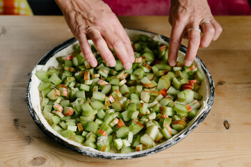 Unrecognizable man baker standing near table and arranging neatly cut green rhubarb pieces on pie dough