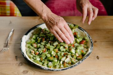 Unrecognizable man baker standing near table and arranging cut green rhubarb pieces on pie dough