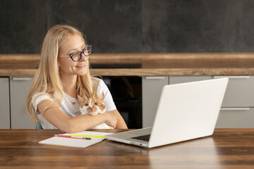 Young woman using laptop and cute cat sitting on the keyboard. Casual girl working on a laptop with her pet while sitting in a homely cozy office.