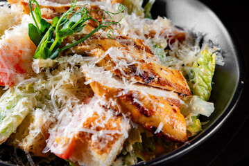 Caesar salad with croutons, cheese, eggs, tomatoes and grilled chicken on black wooden table