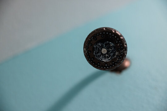 An oil rubbed bronze shower head that needs to be cleaned from a white buildup of dirt, calcium, mineral deposits and hard water