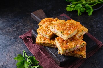 Sliced snack cake with zucchini, ham and cheese on a wooden board on a dark concrete background. Recipes for zucchini.