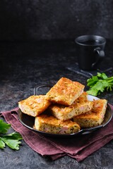 Sliced snack cake with zucchini, ham and cheese on a black plate on a dark concrete background. Recipes for zucchini.