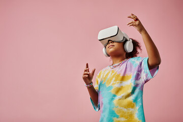 Cute girl in casualwear and VR headset standing in front of camera with copyspace on her right and...