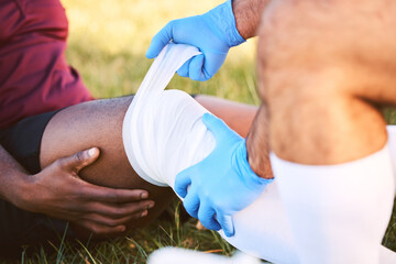 Bandage, knee pain and injury, medic help athlete and sports accident on field with health and wellness. People outdoor, paramedic dressing wound and medical care with inflammation and fracture - Powered by Adobe