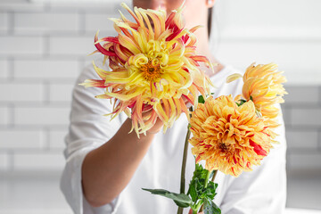 A woman holding a bouquet of yellow and orange dahliason a light background.
