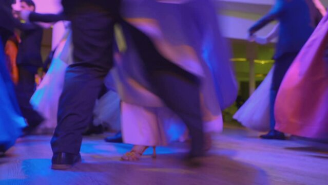 Waltzing pairs dancing a waltz at ball in modern neon lighting. Men are dressed in tailcoat and girls in ballroom long dresses