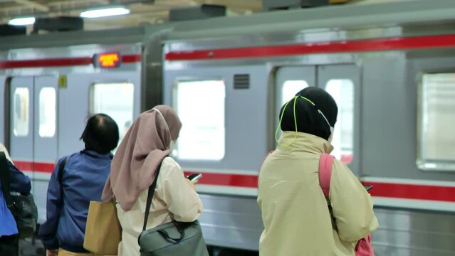 Female passengers waiting for an incoming commuter train at station in Jakarta city at night with departing trains in the background. Depicts the density of train passengers at the station after work 