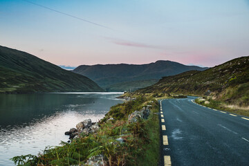 Connemara loop or road as the sun sets on Killary Fjord, Connemara National Park. Western Ireland sunset as the scenic N59 route stretches beside the calm ocean water surrounded by mountains. Ireland