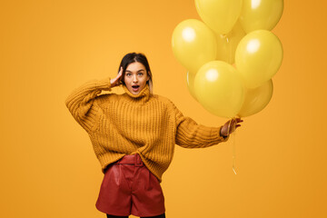 Shocked young lady with yellow balloons looking at camera with astonishment