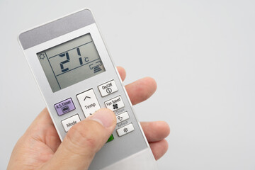 Hand holding air conditioner controller with buttons and display on isolated background.