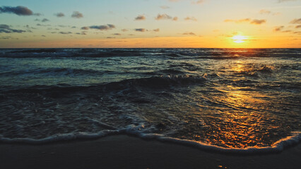 Beautiful sandy beach while sunset. Beautiful seascape of a sandy beach. Sun over horizon and  rolling ocean waves to the shore while sunset. Summer, travel and tourism. Beautiful wild nature.