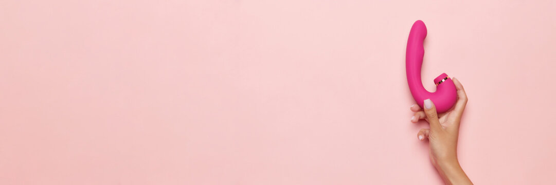 Banner. Female hand with vibrator, medical massager over pastel pink background. Image for sex shop. Concept of woman health, medicine, ad