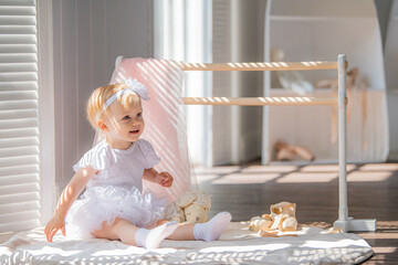 A cute little ballerina in a white ballet costume is sitting near the barre in the room. Kid and ballet dance. Copyspace.