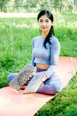 Asian woman holding sadhu boards and sitting on yoga mat at park