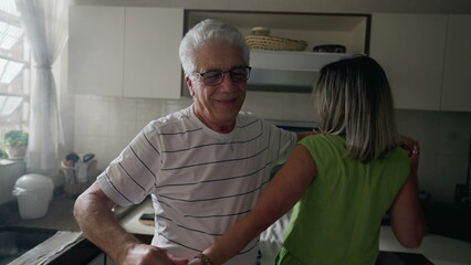 Happy romantic older couple dancing together in kitchen, retired senior enjoying the golden years in joyful embrace and dance