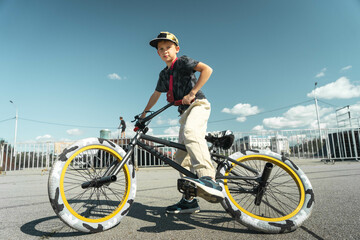 A boy in a cap and T-shirt rides a bmx bike and learns to perform tricks near a special ramp for stunts.