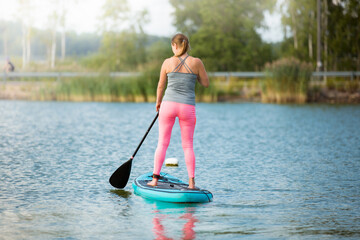 Young athletic woman paddling along the river standing on the sup board