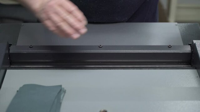 Hands of worker undercutting layers of 2 leather pieces for following processing. Concept of factory production of leather goods