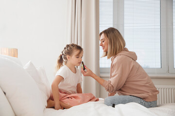 mom and little daughter resting uses essential oils and enjoying fragrance sitting on a bed at...