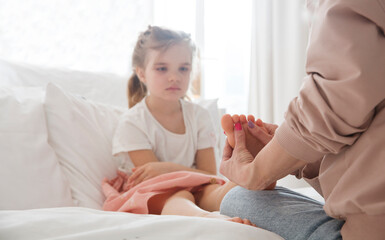 Obraz na płótnie Canvas Mom massages her little daughter's feet with aroma essential oils sitting on the bed at home. Aroma therapy