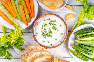 Cottage cheese high-protein dip with fresh vegetables, bread and crackers on wooden white table...