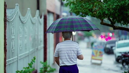 Older man leaving home while raining, opens umbrella and closes gate behind him. Senior walks in street sidewalk